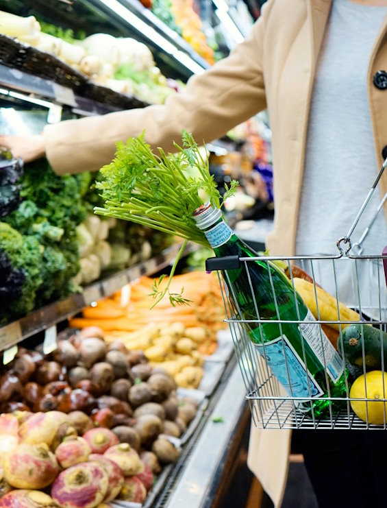 Frau beim Einkaufen im Supermarkt mit einem Einkaufskorb, in dem gesunde Lebensmitteln und eine Flasche Wasser liegen